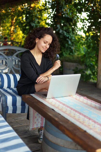 Sensuelle jeune femme travaillant sur un ordinateur portable assis sur la terrasse en regardant la caméra