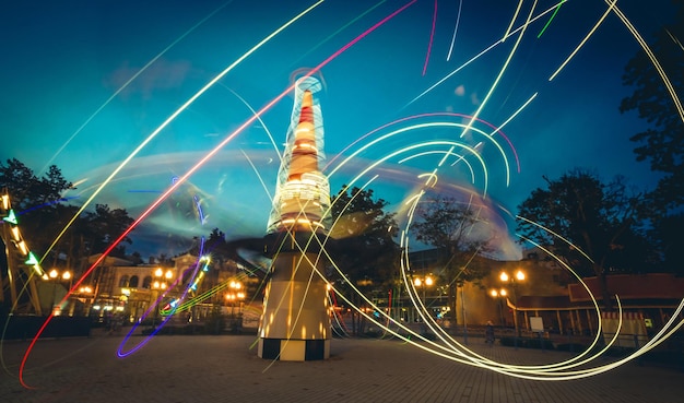 Sentiers lumineux au néon de carrousels dans un parc d'attractions au crépuscule