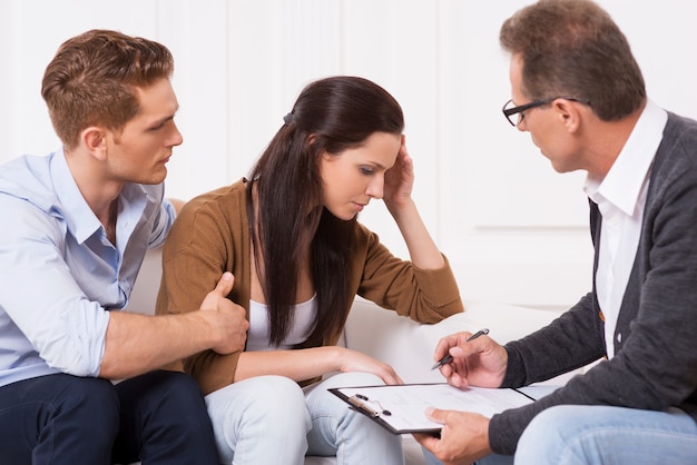 Sentiment de désespoir. Jeune homme consolant sa femme déprimée alors qu'il était assis avec un psychiatre