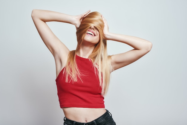 Sentiment d'une femme mince enjouée et heureuse en débardeur rouge couvrant le visage avec ses cheveux