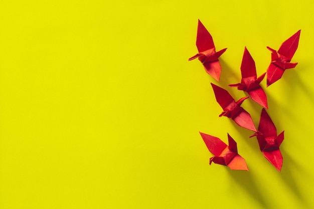 Sept oiseaux origami rouges volent en tête par un oiseau rose, isolé sur blanc, Grue en papier origami rouge