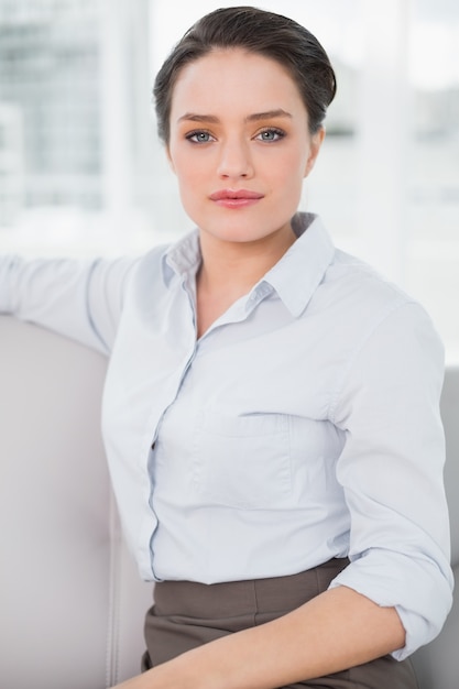 Sérieuse bien habillée jeune femme assise sur le canapé