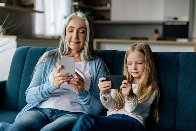 Sérieuse petite fille caucasienne occupée et vieille mamie regarder une vidéo sur ses propres smartphones jouer au jeu utiliser une nouvelle application