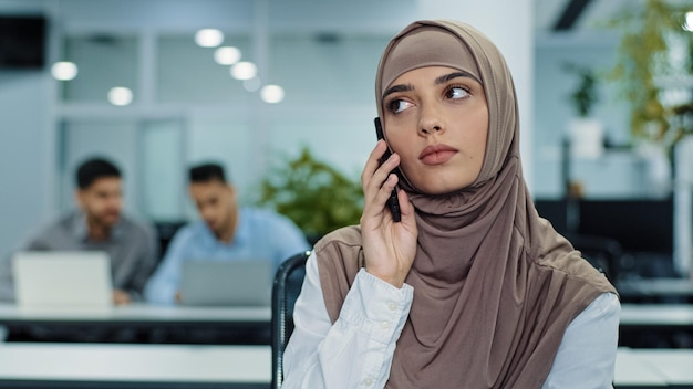 Sérieuse responsable arabe du millénaire en hijab parlant au téléphone consultant faisant un appel d'affaires au travail jeune travailleuse ou cliente parlant par mobile expliquant résoudre le problème