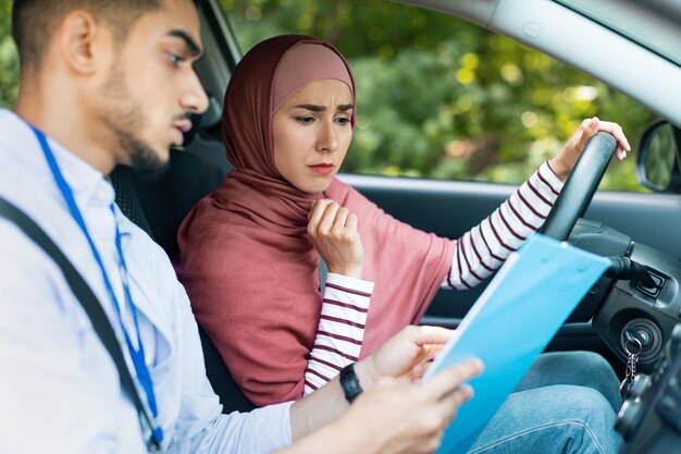 Sérieux beau jeune enseignant musulman montre à une femme pensive en hijab tablette dans l'espace de copie de cabine de voiture