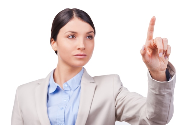 Sérieux et confiant. Jeune femme d'affaires confiante touchant une planche d'essuyage transparente en se tenant debout sur fond blanc