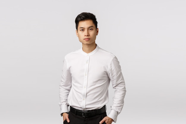 Sérieux, déterminé, prospère homme d'affaires asiatique prospère en chemise blanche, pantalon noir, main dans la poche, appareil photo, écoute du rapport des employés sur les affaires,