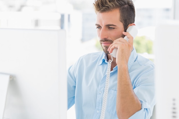 Sérieux jeune homme à l&#39;aide de téléphone et d&#39;ordinateur dans un bureau lumineux