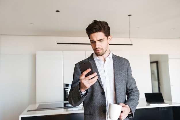 Sérieux jeune homme en costume regardant téléphone mobile