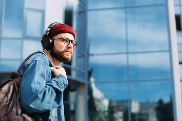Photo sérieux jeune voyageur hipster moderne dans les écouteurs se promène dans la ville. jeu de couleurs bleu. scène urbaine avec espace copie.