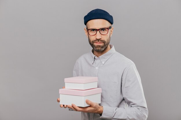 Sérieux modèle masculin habillé dans des vêtements de fête, détient des cadeaux dans les mains, va féliciter un ami avec anniversaire