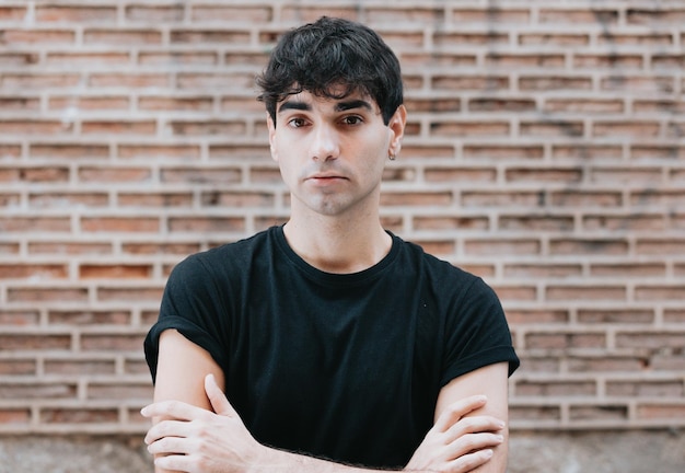 Sérieux à propos de son futur jeune homme caucasien avec une chemise noire regardant la caméra avec un fond de mur de brique orange. Espace de copie. Concept de style de vie, vie urbaine nouvelle sur la ville