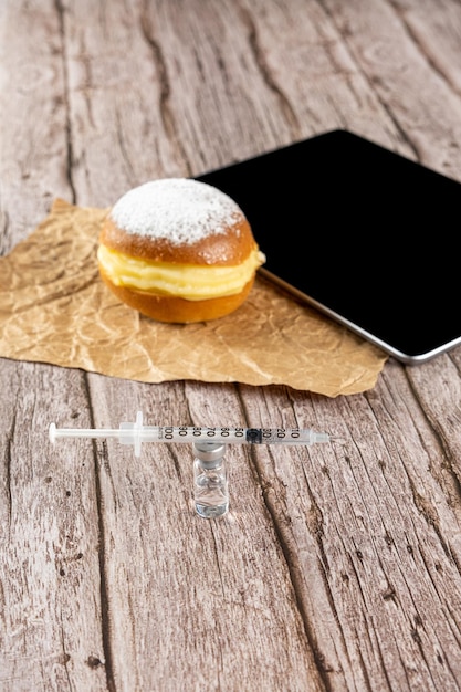 Seringue sur une ampoule d'insuline à côté d'un beignet à la crème brésilienne et d'un comprimé