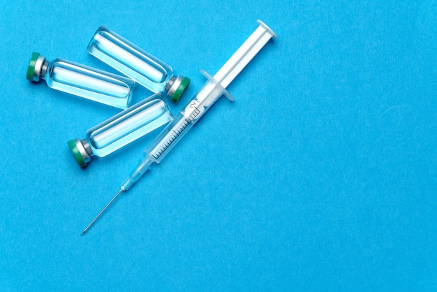 Photo seringue et ampoules avec des médicaments ou des vaccins sur fond bleu