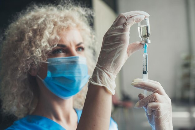 Une seringue en cours d'élaboration avec le vaccin covid closeup portrait femme médecin aux cheveux bouclés vêtu de medi...