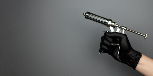 Photo seringue d'injection vétérinaire ou pistolet de vaccination à la main dans une bannière à gants de nitrile noir