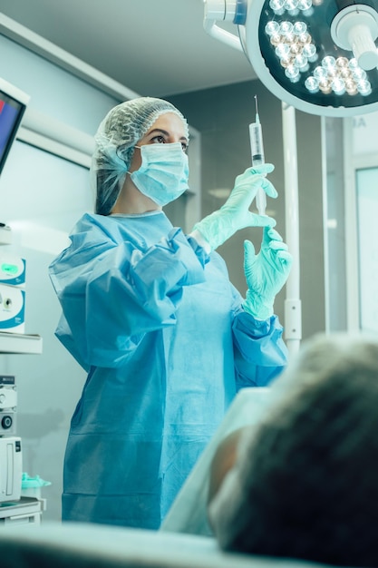 Seringue avec des médicaments dans les mains d'une femme médecin concentrée dans la salle d'opération