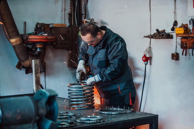 Serrurier dans des vêtements spéciaux et des lunettes travaille dans la production de traitement des métaux avec un spa pour meuleuse d'angle