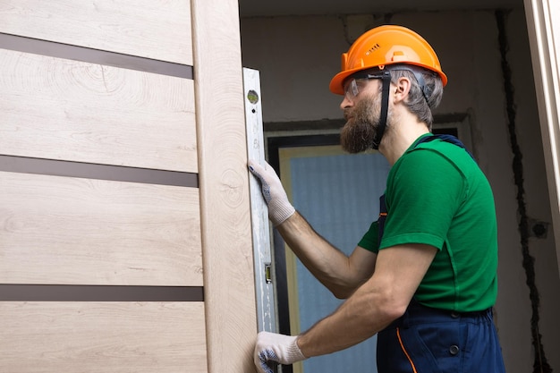 Un serrurier masculin installe une porte dans un appartement Le type vérifie l'exactitude des mesures