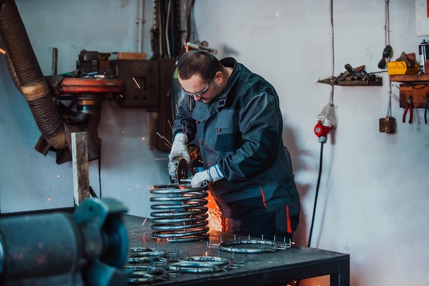 Serrurier en vêtements spéciaux et lunettes travaille en production Traitement des métaux avec meuleuse d'angle Étincelles dans le travail des métaux