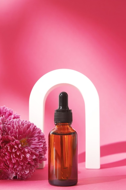 Sérum aux extraits floraux pour les soins de la peau en arche Cosmétiques Nature en bouteille de verre avec pipette et fleurs roses sur fond rose Concept de spa de soins du visage et du corps