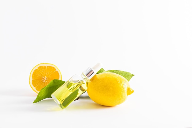 Le sérum de citron pour le visage avec de la vitamine C dans une bouteille transparente avec un compte-gouttes se trouve sur un fond blanc de citron mûr vue de face un espace de copie