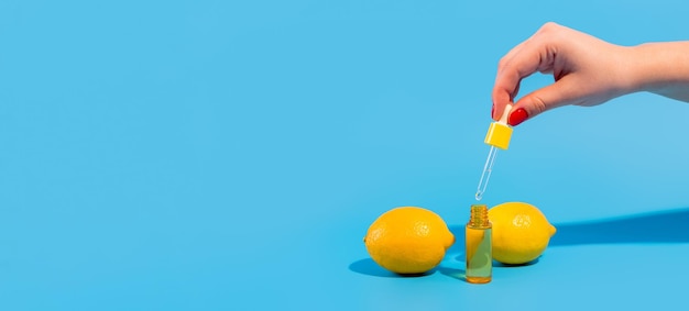 Sérum dans une bouteille transparente avec une pipette tenir la main avec des citrons jaunes sur fond bleu