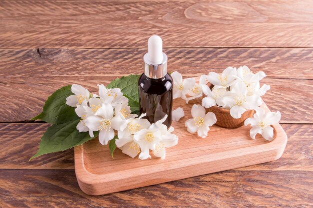 Le sérum facial à l'extrait d'huile de jasmin dans une bouteille cosmétique se dresse sur un plateau en bois parmi des fleurs blanches parfumées soins supplémentaires