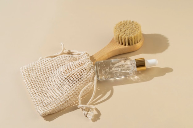 Un sérum organique naturel transparent ou une huile essentielle pour les soins du visage et la brosse de massage du visage allongée sur un fond beige