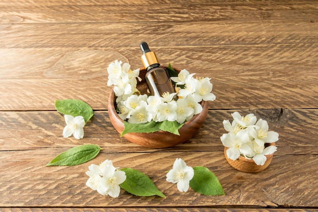 Un sérum pour le soin de la peau du visage et du corps à base d'huile de jasmin se trouve dans un bol en bois parmi des fleurs blanches bio selfcare