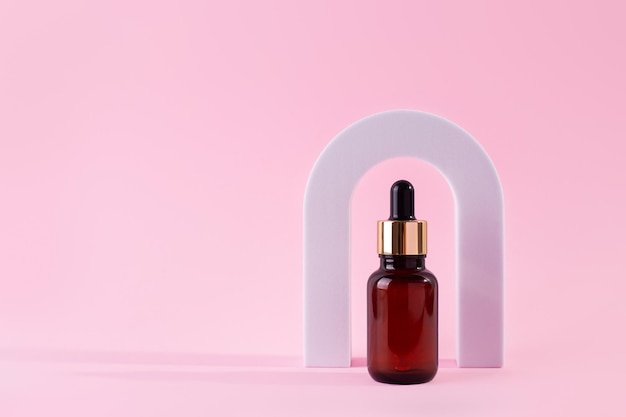 Sérum pour le visage au collagène de beauté dans un flacon compte-gouttes en verre à Arch sur fond rose