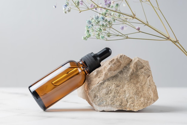 Sérum pour le visage ou huile essentielle dans un flacon compte-gouttes en verre foncé près de la pierre et de la branche séchée de la fleur de gypsophile. Cosmétique de soin de la peau. concept de présentation du produit.