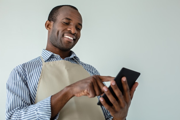 Serveur afro-américain positif souriant en se tenant debout contre le mur blanc