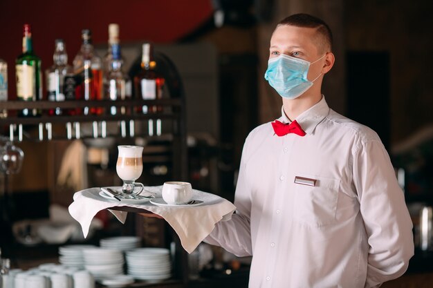 Photo un serveur d'apparence européenne dans un masque médical sert du café au lait.