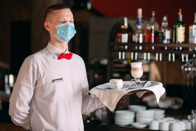 Photo un serveur d'apparence européenne dans un masque médical sert du café au lait.