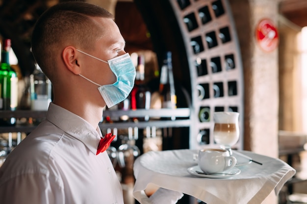 Un serveur d'apparence européenne dans un masque médical sert du café au lait.