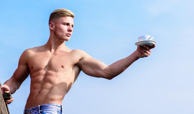 Serveur attrayant de torse sexy. L'homme bodybuilder athlète musclé vous offre du café. Torse nu de poitrine musclée macho tenir une tasse de café frais fond de ciel bleu. La poitrine nue du serveur tient une tasse de café.