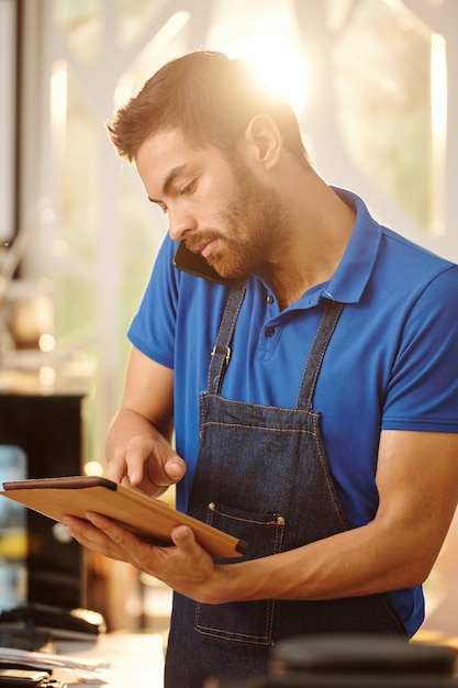 Serveur de café parlant au téléphone avec le client et entrant les informations de commande sur une tablette