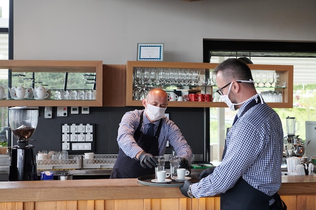 un serveur dans un masque de protection médicale sert le café au restaurant pendant la pandémie de coronavirus représentant un nouveau concept normal