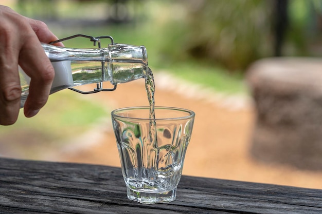 Un serveur dans un restaurant verse de l'eau fraîche d'une bouteille dans un verre en gros plan à l'extérieur