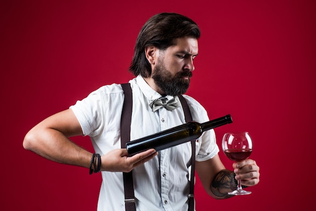 Serveur élégant barman masculin buvant un verre de vin homme barbu en bretelles boire du vin rouge homme d'affaires élégant porter un nœud papillon pour un événement formel sommelier dégustation barman d'alcool