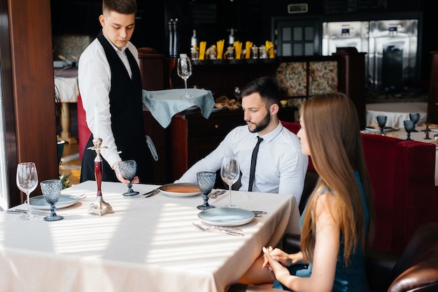 Un serveur élégant sert un jeune couple qui est venu à un rendez-vous dans un restaurant gastronomique. Service à la clientèle dans la restauration.