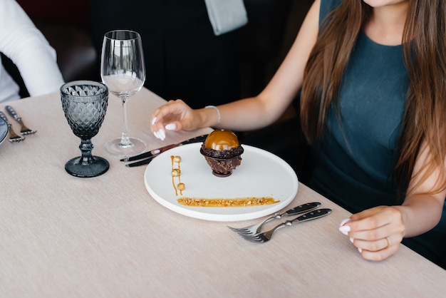 Un serveur élégant en tablier sert une jeune fille dans un bon restaurant et lui sert un dessert unique recouvert d'or alimentaire. Service Clients.