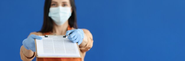 Serveur femme dans un masque médical de protection et des gants donnant un presse-papiers avec des documents et un stylo pour signa...