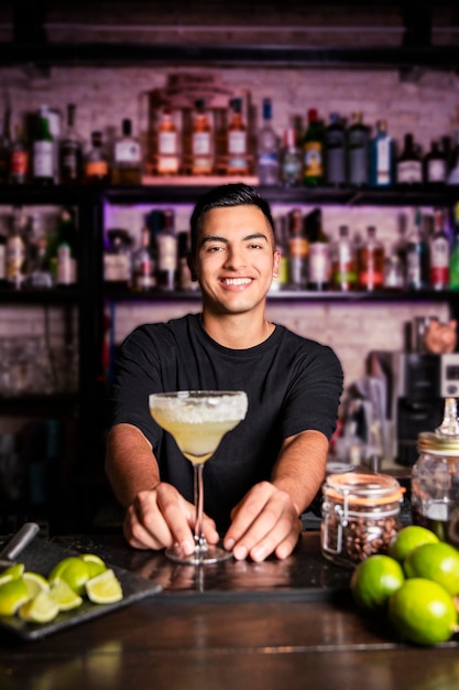 Serveur latino-américain souriant derrière un bar club à côté d'un cocktail margarita