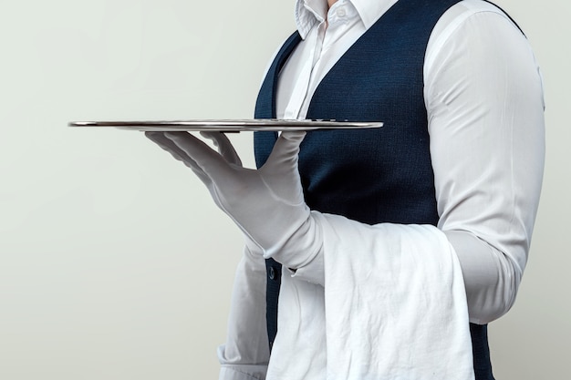 Un serveur masculin vêtu d'une chemise blanche et de gants blancs se tient sur le côté avec un plateau en argent. Le concept de personnel de service au service des clients dans un restaurant.