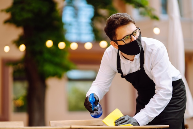 Serveur en masque de protection et gants désinfectant la table du restaurant pour le prochain client.