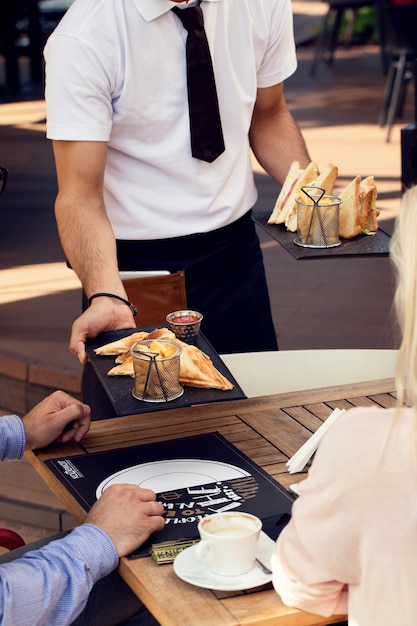 Serveur méconnaissable servant des invités et leur apportant de la nourriture à table dans un restaurant