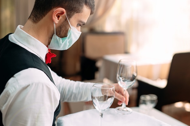 Un serveur portant un masque de protection médical sert la table dans le restaurant