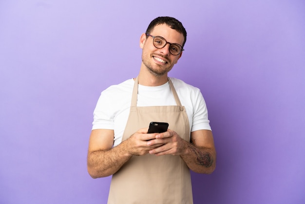 Serveur de restaurant brésilien sur fond violet isolé envoyant un message avec le mobile